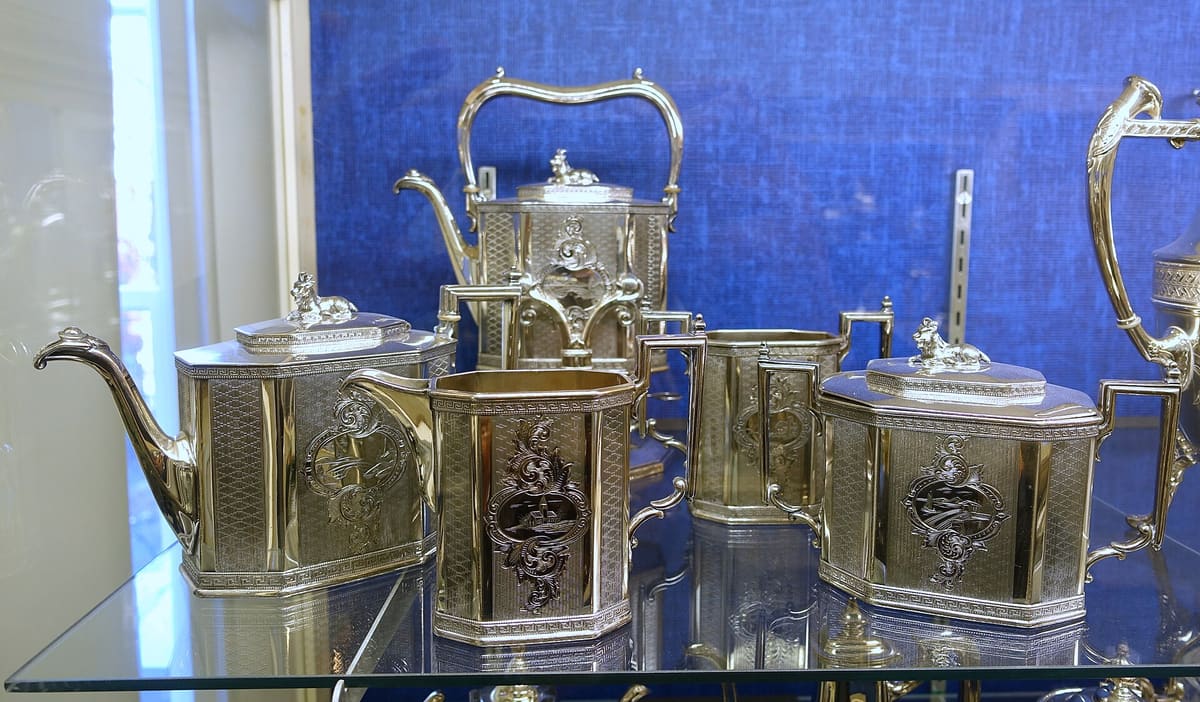 An engraved Victorian silver-plated tea service on a glass shelf