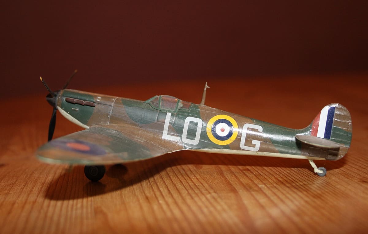 A built Airfix model Spitfire in RAF camouflage on a wooden table