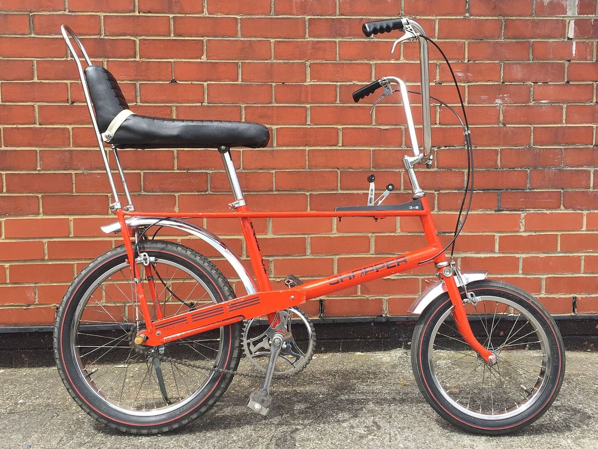 An orange Raleigh Chopper bicycle against a red brick wall